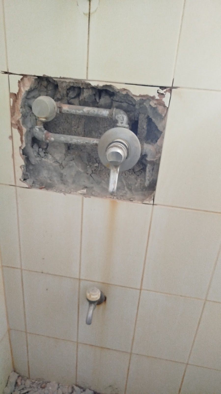 מיקסר סמוי מותקן בתוך קיר אריחים פתוח, כשהצנרת גלויה.